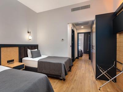 Modern eingerichtetes Hotelzimmer mit zwei Betten, Holzboden und Fernseher an der Wand.