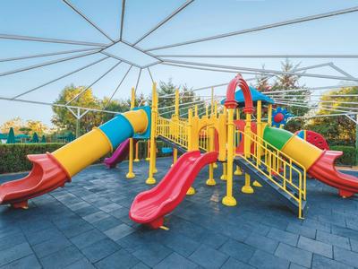 Bunter Spielplatz mit Rutschen, Klettergerüst und weichem Bodenbelag unter blauem Himmel.