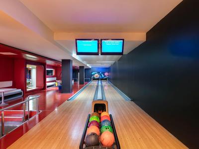 Moderne Bowlingbahn mit zwei Bahnen, bunten Kugeln und großen Monitoren an der Decke.