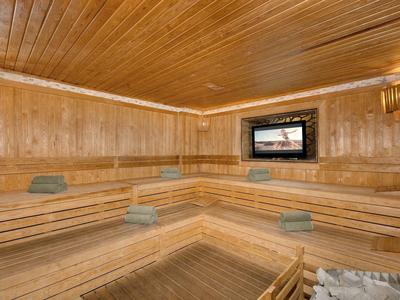 Holzsauna mit Eckbänken, Handtüchern und einem Bildschirm an der Wand.
