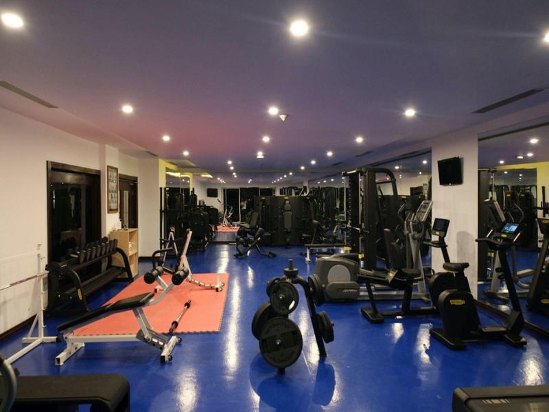 Moderne Fitnessstudio mit verschiedenen Trainingsgeräten, Gewichten und Spiegeln, helle Beleuchtung.