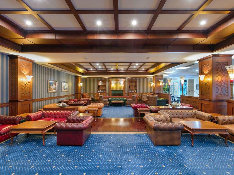 Geräumiger, luxuröser Lounge-Bereich mit Polstermöbeln, Holzvertäfelung und blauem Teppichboden.