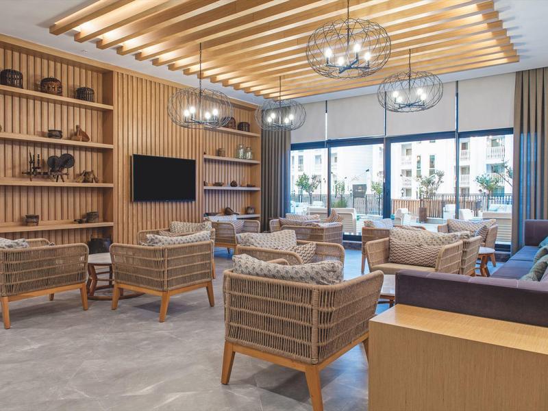 Moderní lounge s dřevěnými akcenty, proutěnými křesly a velkými okny s výhledem na terasu.