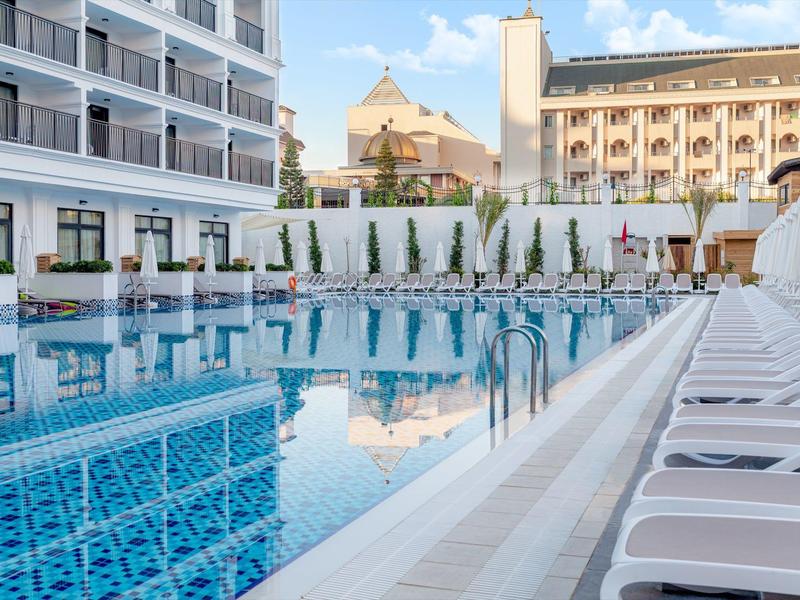 Moderní venkovní bazén s lehátky před hotelovou budovou za denního světla.