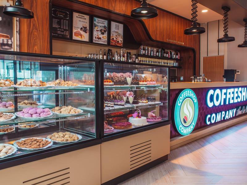 Pekárna a kavárna s osvětlenou výstavní skříní plnou pečiva a dortů.