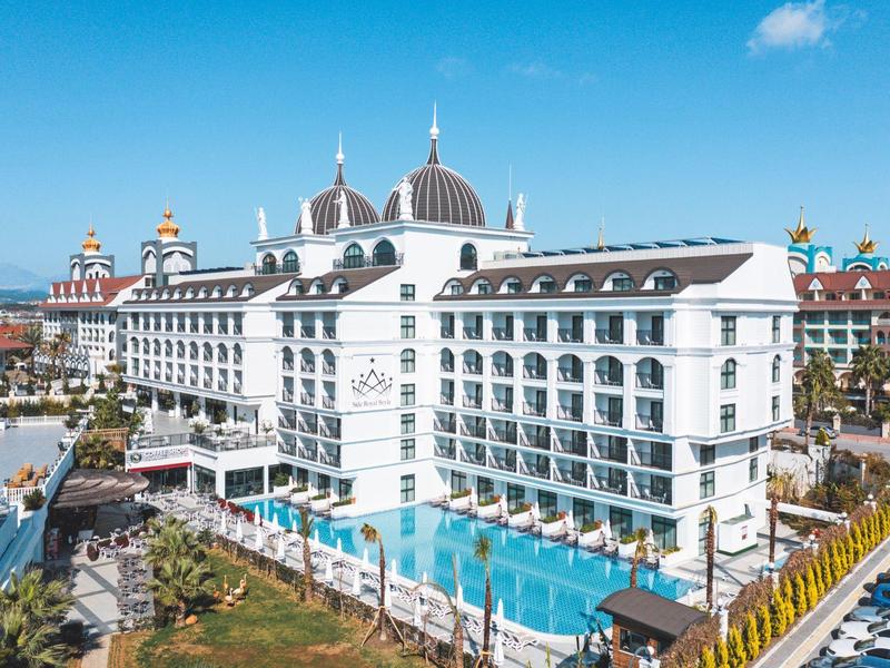 Velký bílý hotel s několika patry a velkým venkovním bazénem za jasné oblohy.