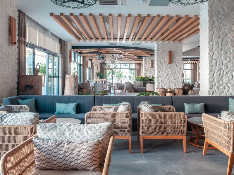 Pohodlný vnitřní prostor s ratanovými židlemi a modrými polštáři v moderním hotelu.