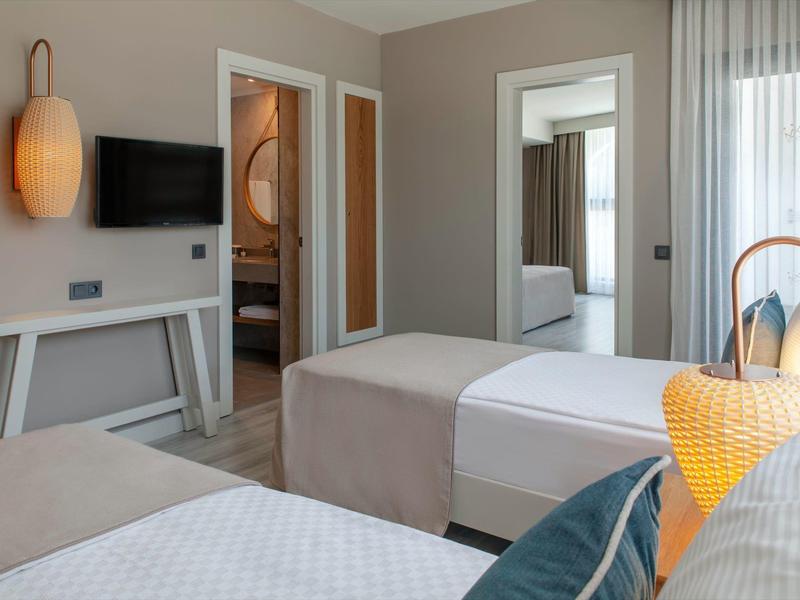 Hotelový pokoj s dvěma postelemi, moderním nábytkem, televizí s plochou obrazovkou a velkým oknem se závěsy.