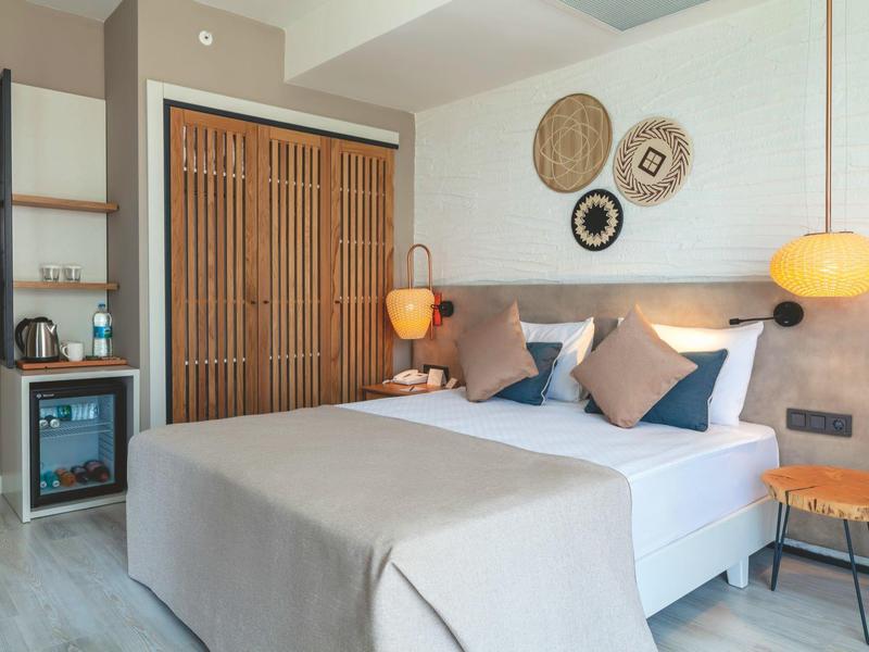 Moderní hotelový pokoj s manželskou postelí, neutrálním dekorací a vestavěným minibarem.