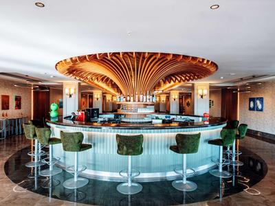 Espace bar circulaire d'hôtel avec tabourets verts rembourrés et éclairage décoratif au plafond.