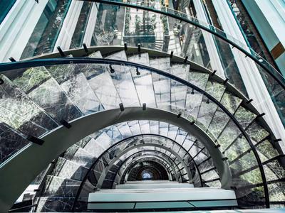 Escalier en colimaçon moderne avec rambarde en verre dans un immeuble haut offrant une vue sur la ville.