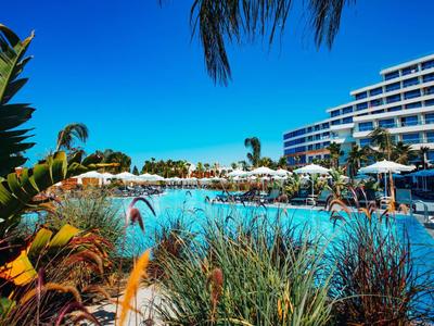 Großer Pool mit klarblauem Wasser, Palmen und Hotelgebäude bei sonnigem Himmel.