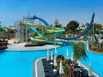 Parco acquatico con scivoli d'acqua blu e verdi e piscina limpida sotto il cielo azzurro.