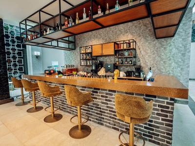 Area bar moderna in hotel con bancone in legno, cinque sgabelli e scaffali con bevande.