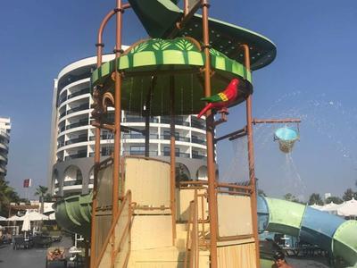 Des enfants jouent dans le parc aquatique avec des toboggans et un carrousel d'eau sous un ciel bleu.