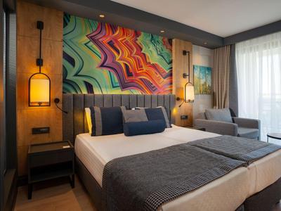 Camera d'hotel moderna con letto grande, arte murale colorata e zona soggiorno accogliente in luce naturale.