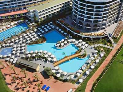 Hotel di lusso con due grandi piscine, numerosi ombrelloni e lettini accanto a un giardino curato.