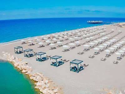 Ampia spiaggia sabbiosa con file di lettini bianchi e mare azzurro sullo sfondo.