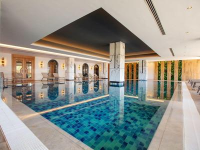 Piscina interna moderna in hotel con pavimento piastrellato blu e comode aree salotto.