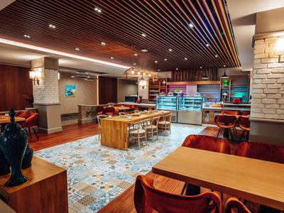 Zona pranzo moderna con tavoli in legno, sedie e soffitto decorativo.