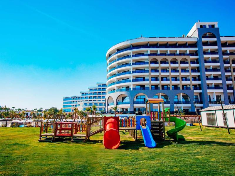 Complexe hôtelier moderne avec aire de jeux sur pelouse soignée sous un ciel bleu.