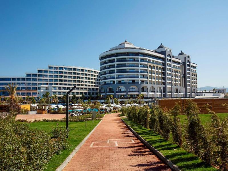 Complexe hôtelier moderne à plusieurs étages, entouré de jardins paysagers et ciel bleu clair.