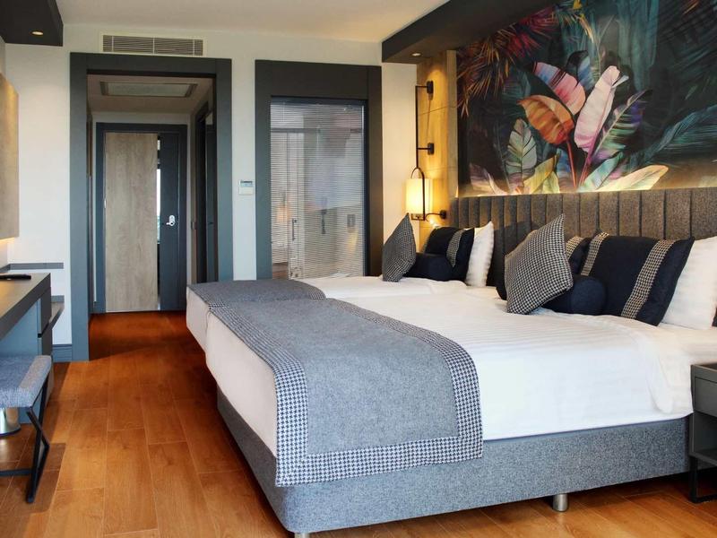 Chambre d'hôtel moderne avec grand lit, meubles en bois foncé et décoration murale colorée.