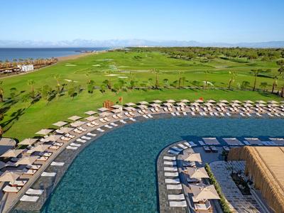 Gran piscina con tumbonas y sombrillas junto a un extenso campo de golf verde bajo un cielo despejado.