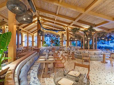 Restaurante moderno y luminoso con techo de madera, grandes plantas y áreas de asientos diversas.