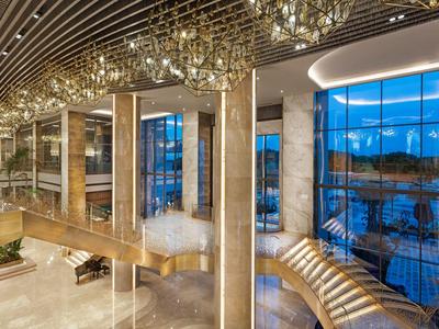 Elegante recepción de hotel con grandes ventanales y candelabro moderno, vista al agua al fondo