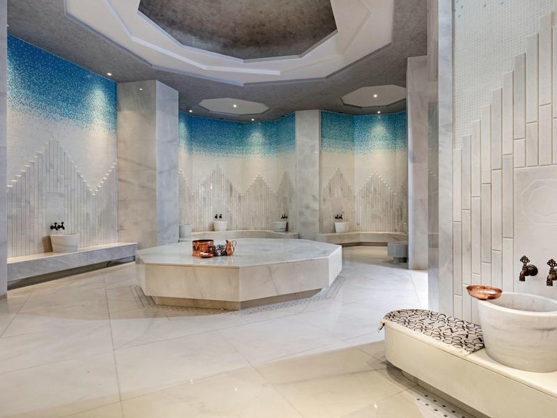 Espacio de spa moderno y lujoso con paredes de mármol, fuente de baño central y luces azules de acento.