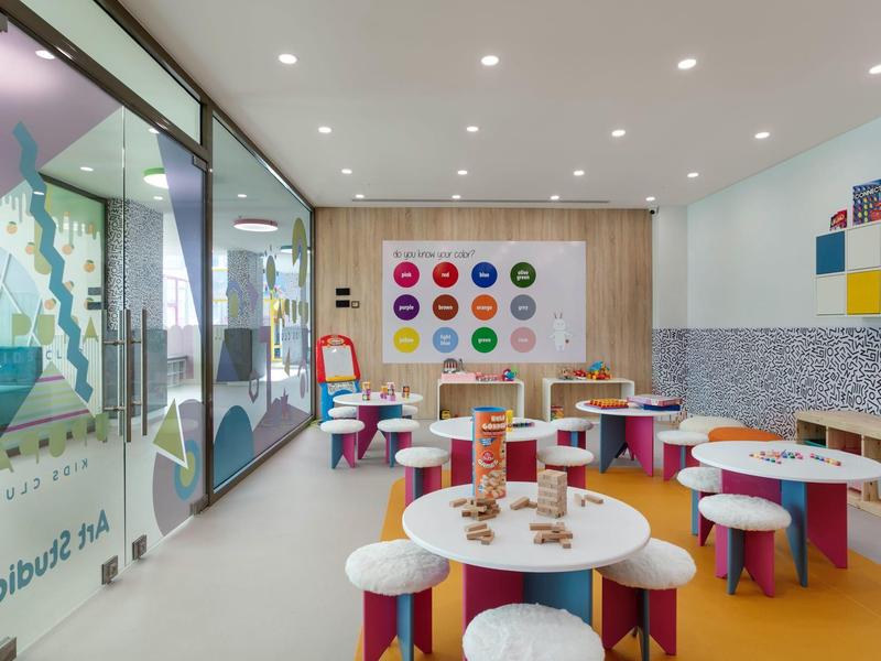 Sala de juegos infantil colorida con mesas, sillas y decoración alegre en un hotel.
