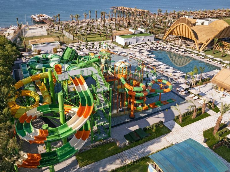 Toboganes de agua y piscinas en un resort animado junto al mar con tumbonas y decoración de palmeras.