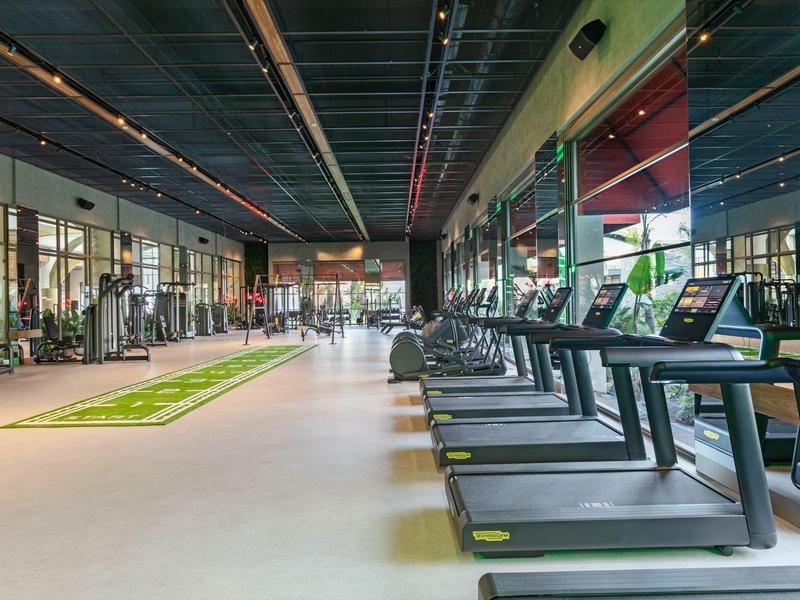 Gimnasio moderno con cintas de correr y pesas en un espacio amplio y luminoso con grandes ventanas.