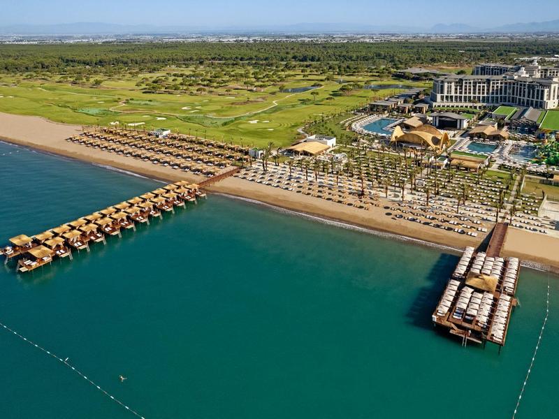Vista aérea de un resort con muelles y villas sobre el agua en un mar azul claro.