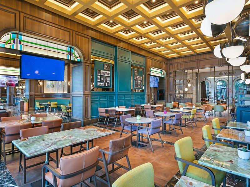 Restaurante moderno con techo de madera, paredes azules y mobiliario mixto con luz cálida.