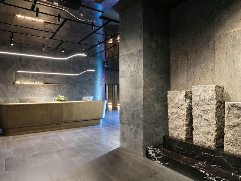 Recepción de hotel moderna con mostrador y pared decorativa de piedra gris y chimenea