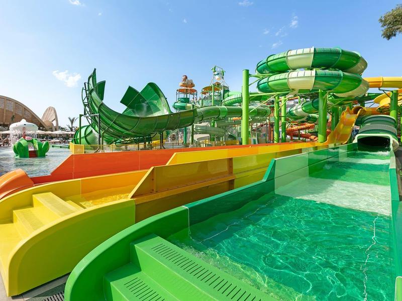 Toboganes de agua coloridos en un gran parque acuático bajo un cielo azul.