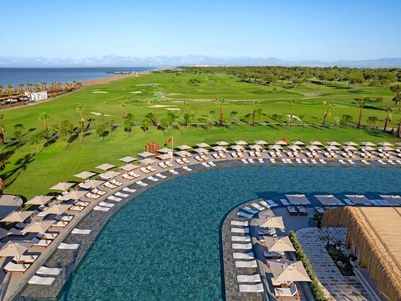 Gran piscina con tumbonas y sombrillas junto a un extenso campo de golf verde bajo un cielo despejado.
