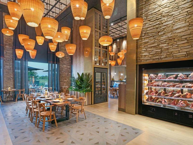 Restaurante moderno con luz cálida, muebles de madera y una gran vitrina de vinos.