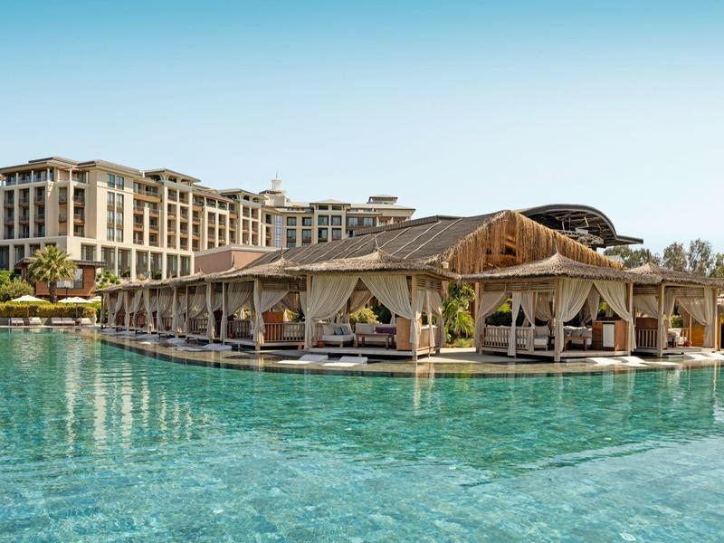 Hotel de lujo con piscina exterior y áreas lounge techadas bajo un cielo despejado.