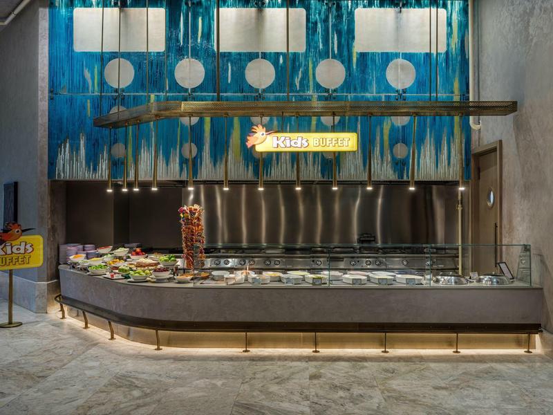 Buffet moderno en hotel con pared azul vibrante y ensaladas frescas en primer plano.