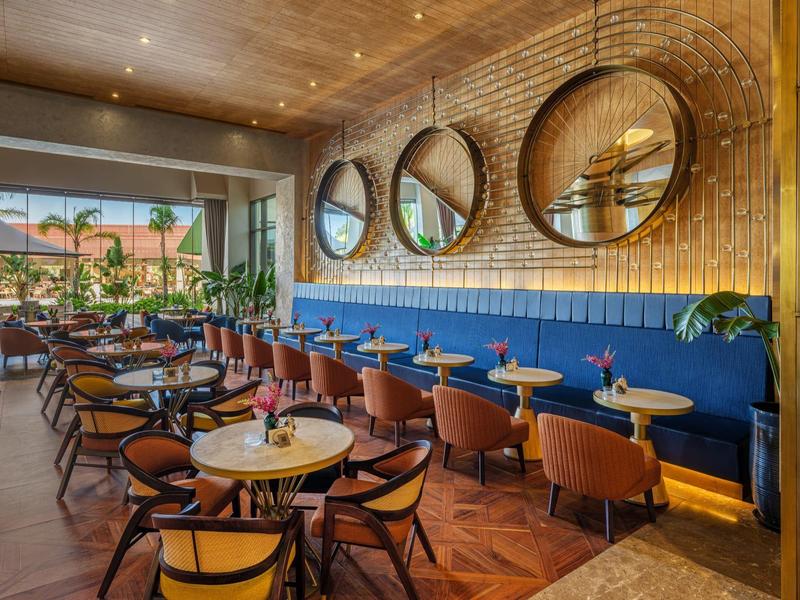 Restaurante de hotel luminoso con espejos redondos, techo de madera y áreas de asiento cómodas junto a ventanas panorámicas.