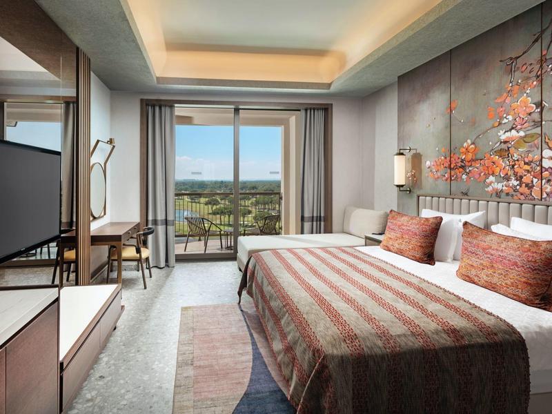 Habitación de hotel moderna con cama grande, balcón y vista a paisaje verde.