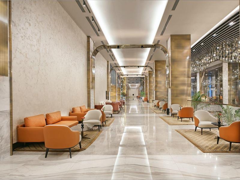 Lobby elegante de hotel con cómodos sillones naranjas, mesas y suelo de mármol liso a lo largo del pasillo.