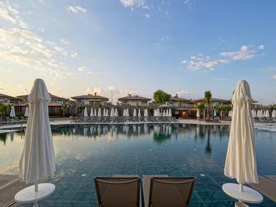 Duży basen hotelowy z leżakami i zamkniętymi parasolami o zachodzie słońca.