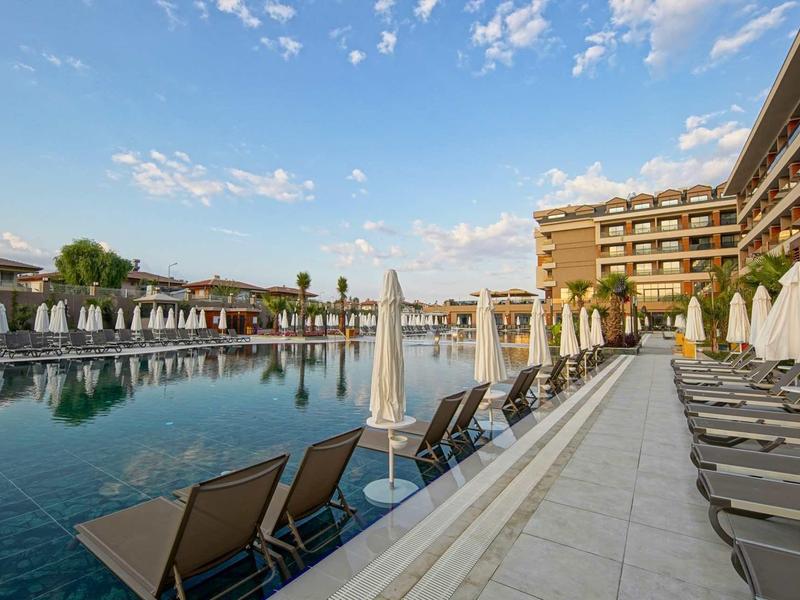 Duży basen hotelowy z leżakami i parasolami pod niebieskim niebem.