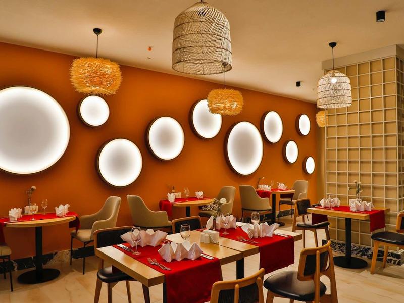 Nowoczesna restauracja z okrągłymi światłami ściennymi i czerwonymi stołami.