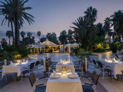 Terrasse de restaurant éclairée au crépuscule avec tables et palmiers.