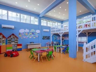 Salle de jeux colorée pour enfants avec tables, chaises, jouets et décoration murale.
